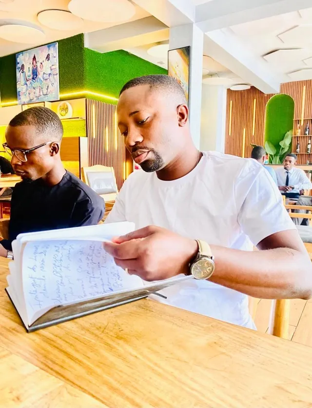 Deux hommes consultent un registre, assis à une table de travail.